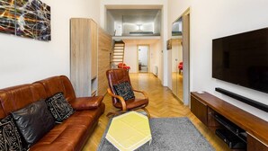 Een moderne woonkamer met een bruine leren bank, een houten stoel, een flatscreen televisie en een trap naar een hoger niveau.