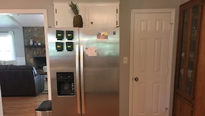 Un réfrigérateur en acier inoxydable doté d’un distributeur d’eau, surmonté d’un ananas et orné d’aimants sur la porte.
