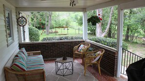Une véranda aménagée avec des meubles en osier, une petite table et une vue sur un jardin.
