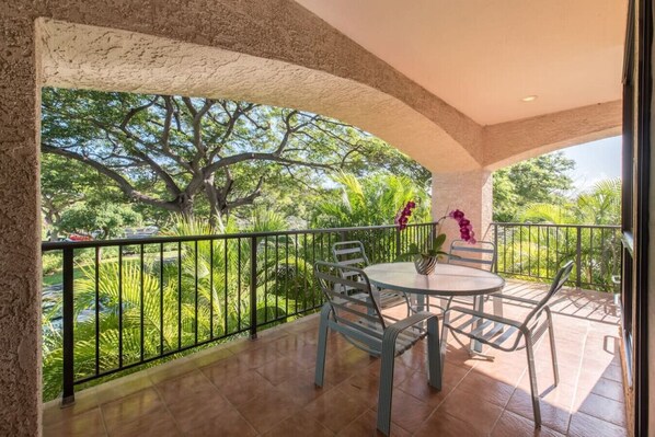 Un balcón con vistas a vegetación exuberante y árboles, una mesa redonda con sillas y una orquídea en maceta.