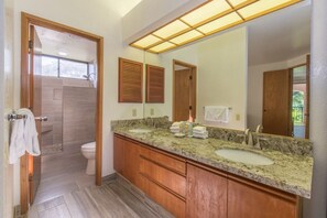 Un baño con tocador de madera, dos lavamanos, un espejo grande y zona de ducha.
