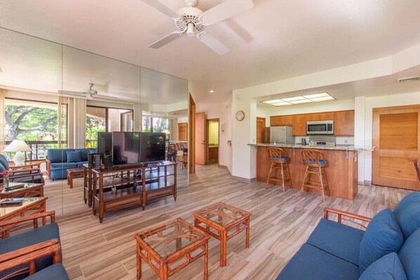 A spacious living room with a large TV, wooden furniture, and a kitchen area with a bar.