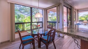 Un comedor con una mesa redonda de cristal, cuatro sillas de madera con cojines azules y una lámpara colgante.