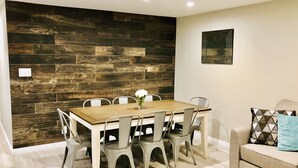 A dining area with a wooden table and chairs, a decorative wall, and a sofa with cushions. - Family-Friendly, Renovated Suite (Extra Cleaning) (Orem)