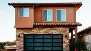 A two-story house with a stone facade, a garage, and a small porch. - Steps to the Beach! Rooftop Deck! Firepit & BBQ! (Oceano)