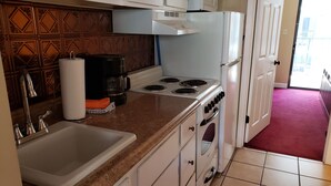 A compact kitchen with a sink, stove, and oven, a coffee maker, and a patterned backsplash.
