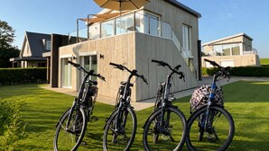 Moderni talo, jossa on suuri lasi-ikkuna, puinen julkisivu ja polkupyörä pysäköitynä etupihalle.