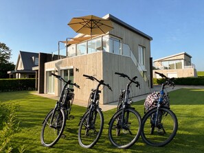 Une maison moderne dotée d’une grande baie vitrée, d’une façade en bois et d’un vélo garé dans le jardin.