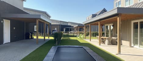 Un patio con un trampolín, un espacio de estar techado y un coche estacionado al fondo.