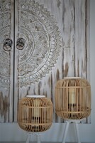 Dos lámparas de mimbre sobre peanas blancas frente a una pared rústica con un motivo circular decorativo.