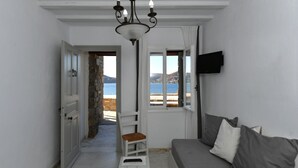 Ein Zimmer mit Meerblick, eine weiße Tür, ein weißer Stuhl, eine Couch mit Kissen und eine Chandelüster.