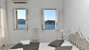 Ein Schlafzimmer mit einem Bett, zwei Fenstern, einem Nachttisch und einem Sessel.