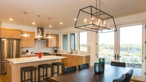 A modern kitchen with a large island, bar stools, and a dining table with chairs. - Luxury + views ~ 7 mins to downtown ~ resort ~ hot tub ~ wifi ~ BBQ ~ Bend ~ 🐶 (Bend)