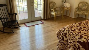 A room with a wooden floor, a rocking chair, two upholstered chairs, a small table with a vase, and a bed with a patterned bedspread. - The Charming Country Cottage-Welcomes you and your pet! (La Plata)