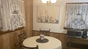 A dining area with a round table, chairs, a chandelier, and a painting of sailboats on the wall. - The Charming Country Cottage-Welcomes you and your pet! (La Plata)