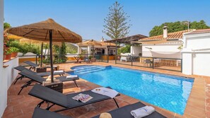 A swimming pool with lounge chairs, a thatched umbrella, and a white building with a tiled roof. - Espina Rural Almogía by Ruralidays (Málaga)