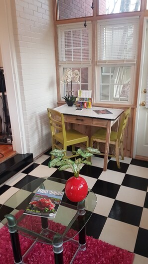 Un coin repas avec un sol à carreaux, une table entourée de chaises, un vase rouge et un magazine posé sur la table.