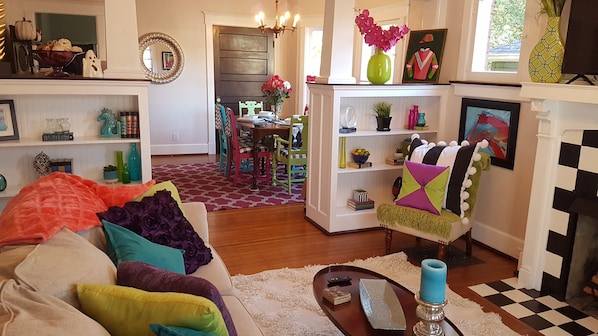 Un salon chaleureux avec un canapé, une table basse et une cheminée. Au fond, on aperçoit un coin repas avec une table et des chaises.