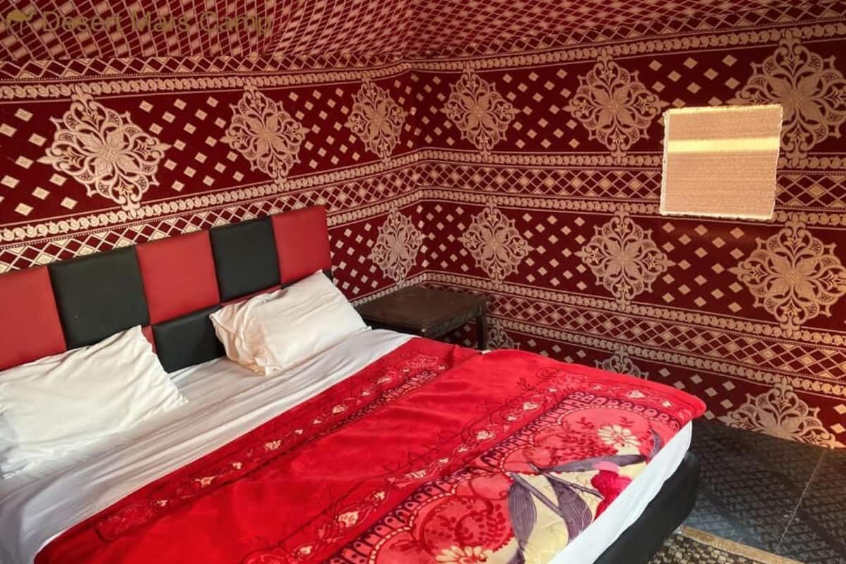A bed with a red and white bedspread, a black headboard, and a patterned wall.