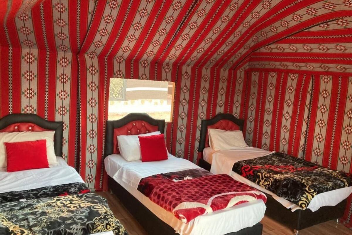 A room with three beds, each with a different patterned bedspread. The room has a striped red and white wallpaper.