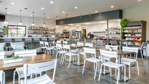 A modern restaurant with white chairs and tables, a bar area, and shelves stocked with bottles and snacks. - Bring your 🚲~ resort pool ~ amenities ~ trails ~ golf ~ hot tub ~ Bend ~ 🐶 (Bend)