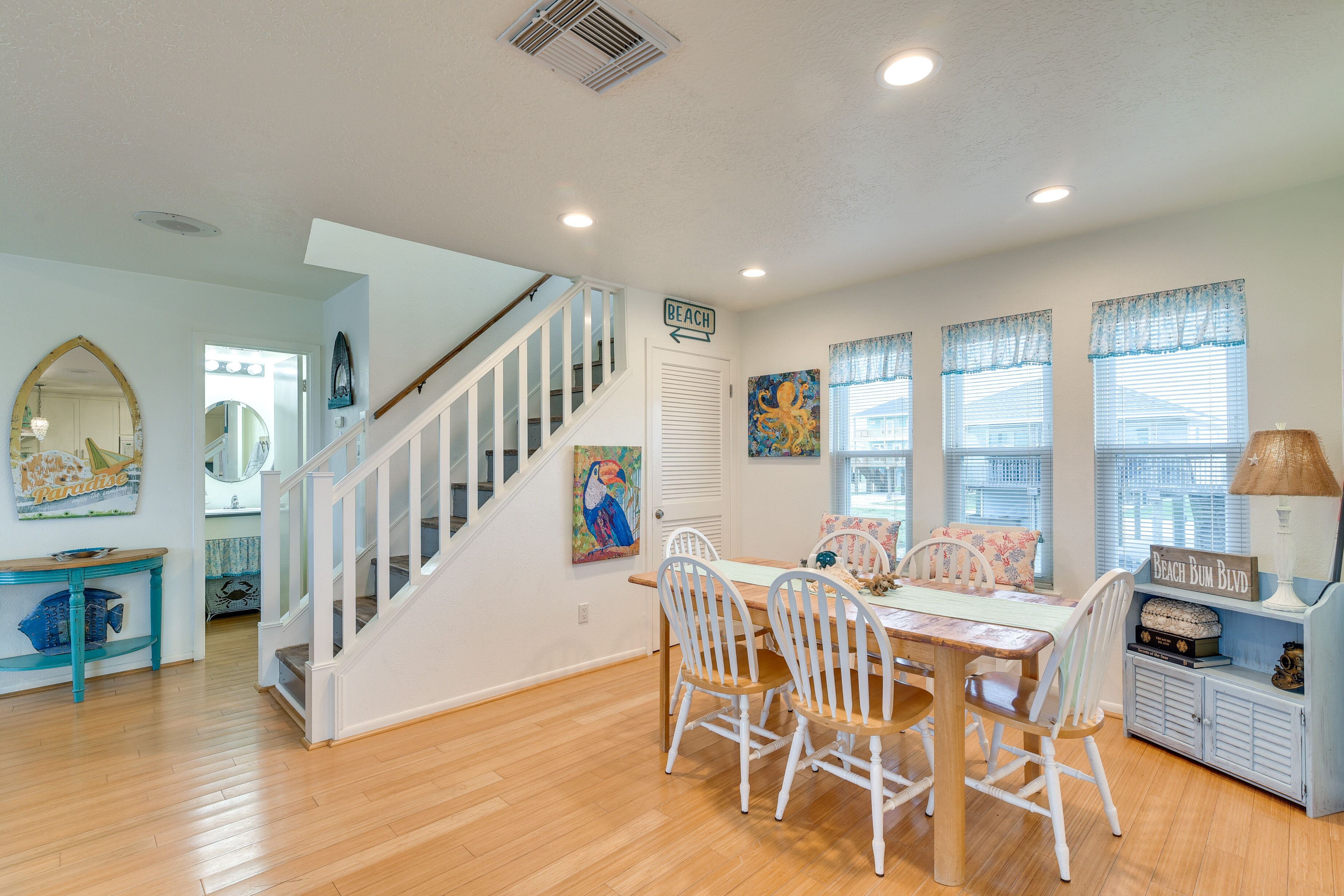 A dining area with a wooden table and white chairs, a staircase with white railings, and a sign indicating 'BEACH'.