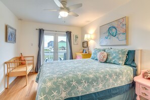 A bedroom with a bed, a nightstand, a desk, a chair, a ceiling fan, and a window with curtains. - Pet-Friendly Condo w/ Seasonal Pool in Galveston! (Galveston)