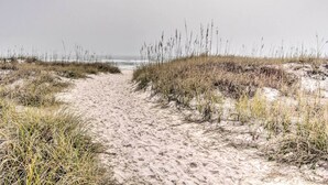 Ein sandiger Küstenpfad mit Grasrändern, der zum Meer führt.