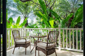 Relax on the balcony surrounded by lush tropical foliage, featuring a wicker chair and small table.
