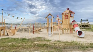 A beach playground with wooden structures, including a slide and climbing frames.