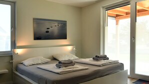 A modern bedroom with a large bed, a ceiling light, a wall-mounted artwork, and a sliding glass door leading to an outdoor area.