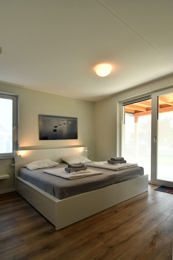 A modern bedroom with a large bed, a ceiling light, a wall-mounted artwork, and a sliding glass door leading to an outdoor area. - Maroma REGAL Exclusive Luxury Vacation Villa near Lake Veere—4 Free E-bikes (Kamperland)