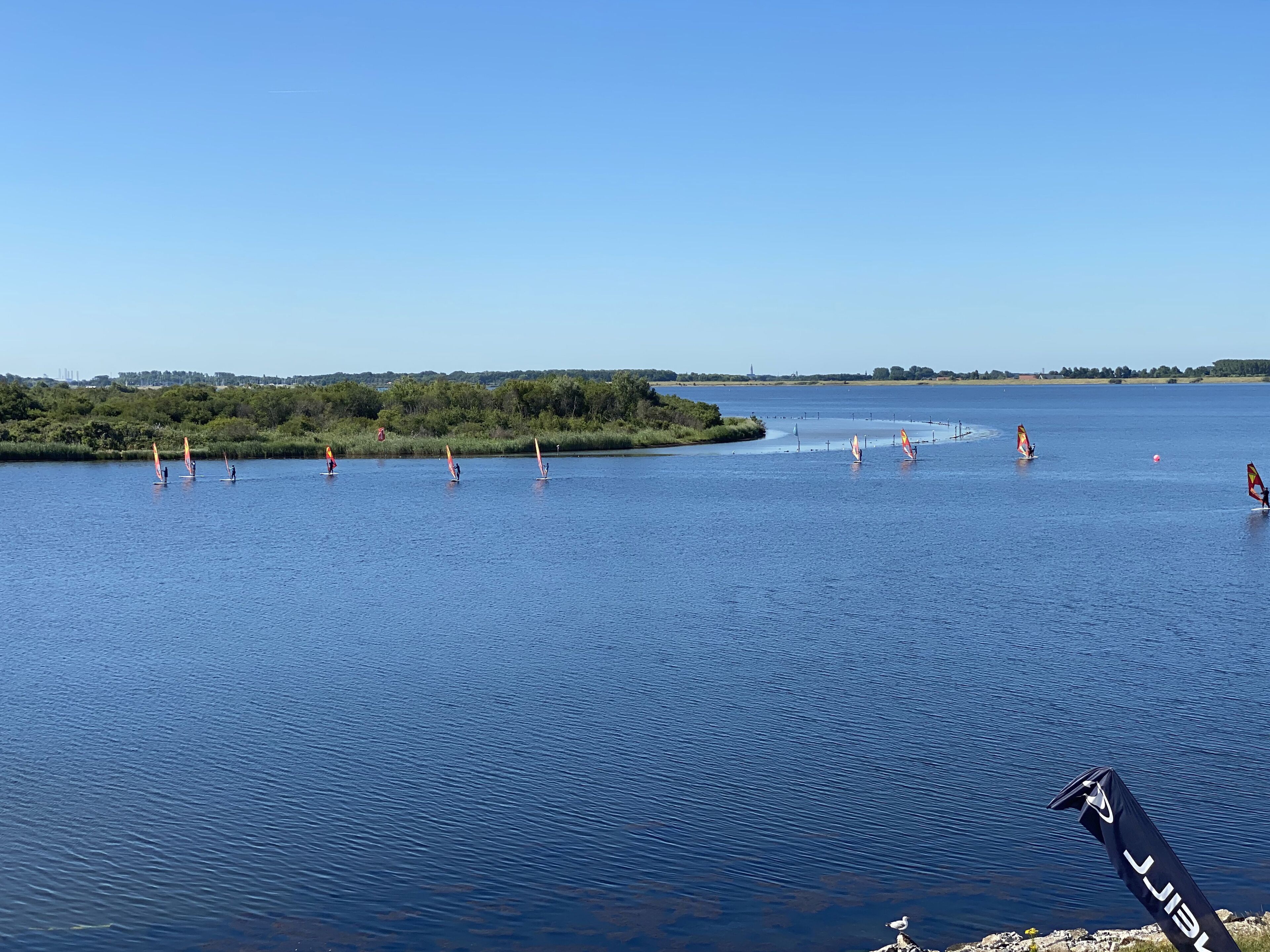 Un lac paisible où l’on pratique la planche à voile, avec un drapeau flottant sur la rive.