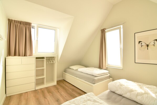 Un dormitorio con techo inclinado, armario empotrado, cama y ventana con cortinas.