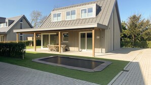 Ein modernes Haus mit überdachter Terrasse, Schwimmbad und gepflegtem Rasen.