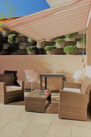 An outdoor patio with wicker furniture, a glass-top table, and a striped awning. - Mini apartment with terrace (without kitchen!) (Dino-Lugano)