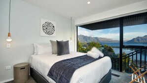 A bedroom with a large bed, a view of mountains and a lake, and a balcony with a railing.