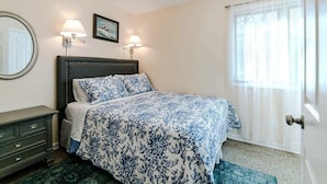 A bedroom with a bed, bedside lamps, a wall-mounted mirror, a framed picture, and a window with curtains. - Dog-Friendly Cottage with Hot Tub (Pullman)
