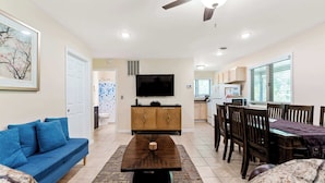 A living room with a blue sofa, a wooden coffee table, a TV, and a dining area with a table and chairs. - Dog-Friendly Cottage with Hot Tub (Pullman)
