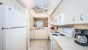 Una cocina compacta con electrodomésticos blancos, una isla central y un ventilador de techo.