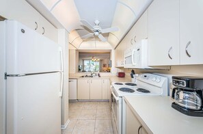 Une cuisine de taille réduite avec des appareils électroménagers blancs, un îlot central et un ventilateur de plafond.