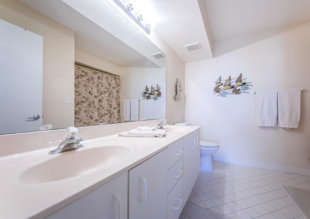 Un baño moderno con un espejo grande, dos lavamanos, un inodoro y decoración en la pared.