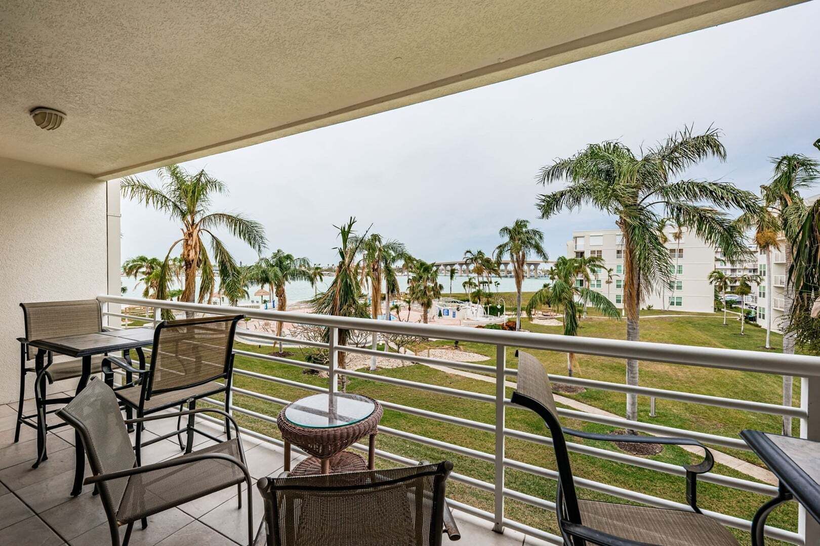 Un balcón con vista a una playa y palmeras, amoblado con sillas y una mesa.
