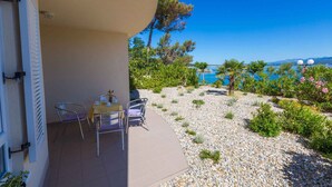 A balcony with a table and chairs, overlooking a pebble garden and a clear blue sea. - Holiday apartment with sea view and barbecue facilities (Šilo)