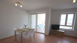 A spacious room with a dining area, a TV, and a sliding glass door leading to an outdoor balcony. - Holiday apartment with sea view and barbecue facilities (Šilo)