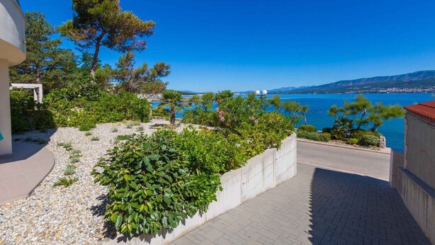 A coastal property with a paved driveway, a landscaped garden with various plants, and a view of the sea and distant mountains. - Holiday apartment with sea view and barbecue facilities (Šilo)
