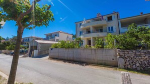 A multi-story residential building with balconies, a paved driveway, and a stone wall. - Holiday apartment with sea view and barbecue facilities (Šilo)