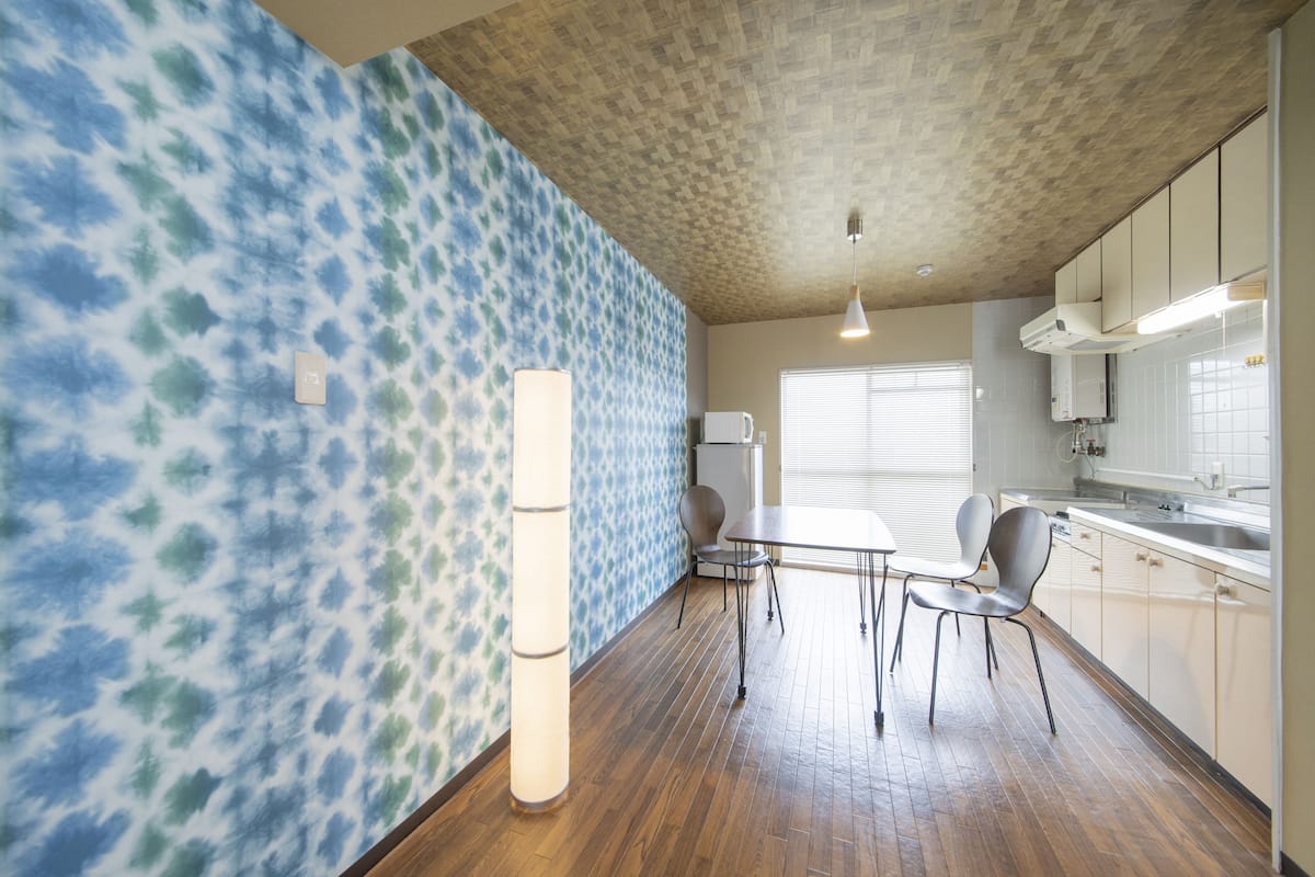 A kitchen with wooden flooring, white cabinets, and a window with blinds.