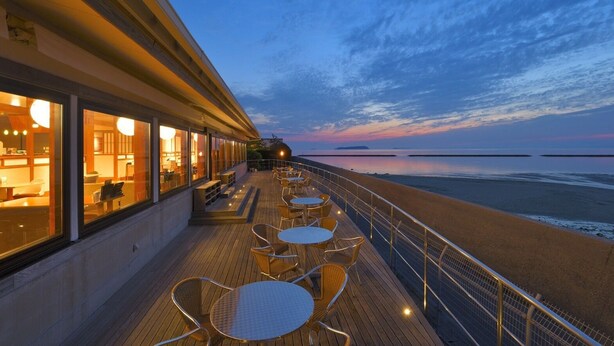 A deck with outdoor seating overlooking a beach at dusk. - Sanuki mansion (Kanonji)