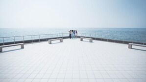 A spacious outdoor area with a tiled floor and benches, overlooking a body of water. - Sanuki mansion (Kanonji)